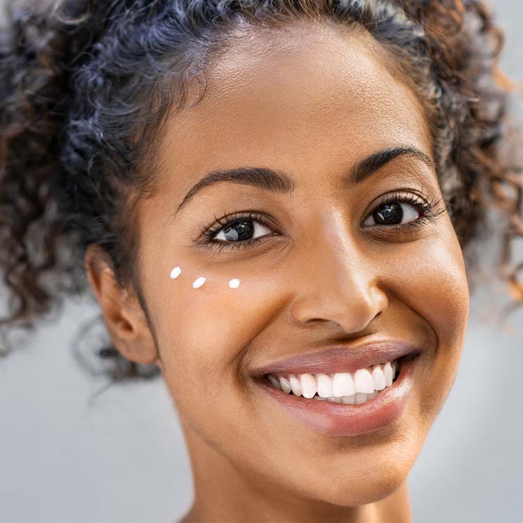 Foto einer schwarzen Frau mit krausem Haar und Augencreme im Gesicht